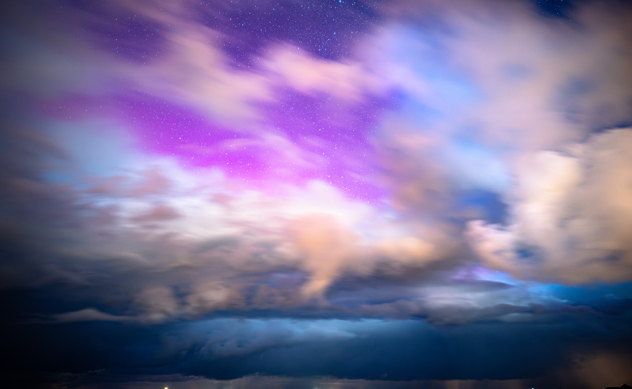 Aurore boréale illuminant un ciel nocturne aux nuances violettes et bleutées, avec des nuages en mouvement offrant un contraste saisissant.