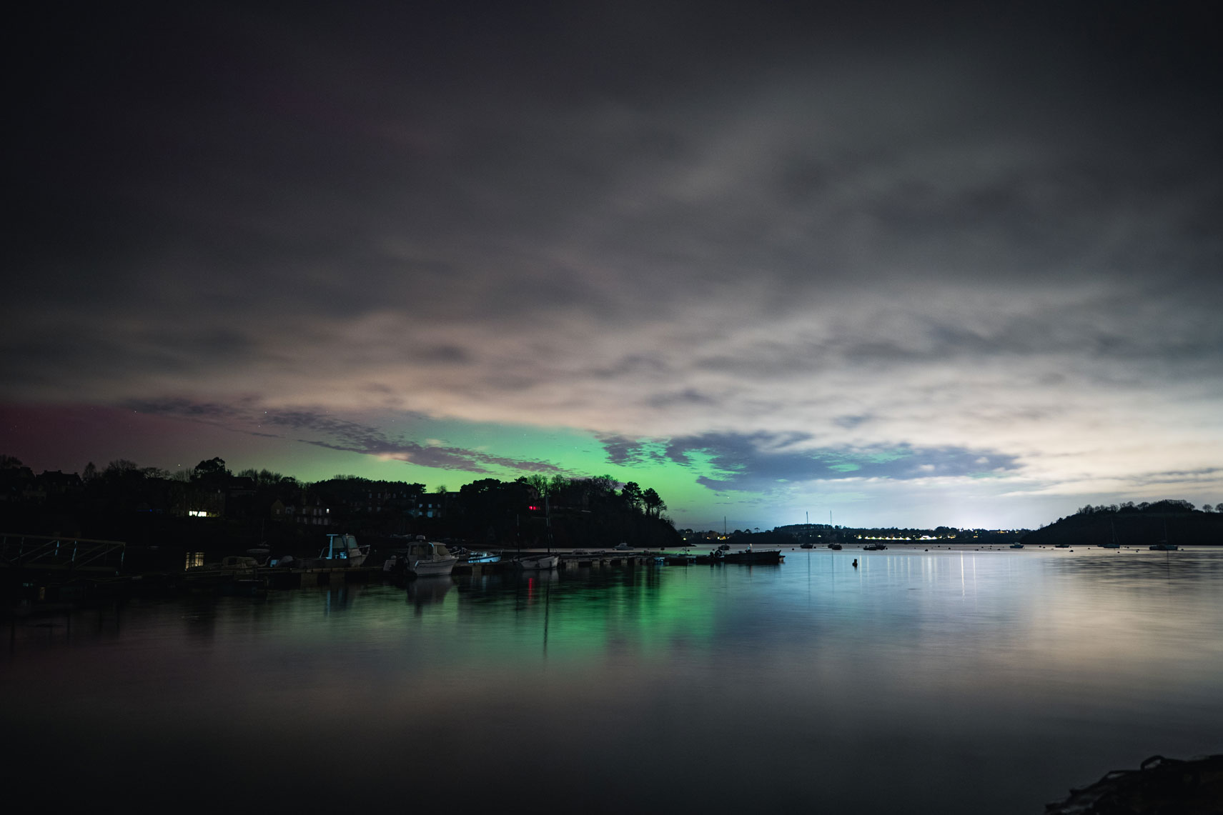Aurores boréales en Bretagne avec reflets calmes sur l’eau et ambiance nocturne apaisée.