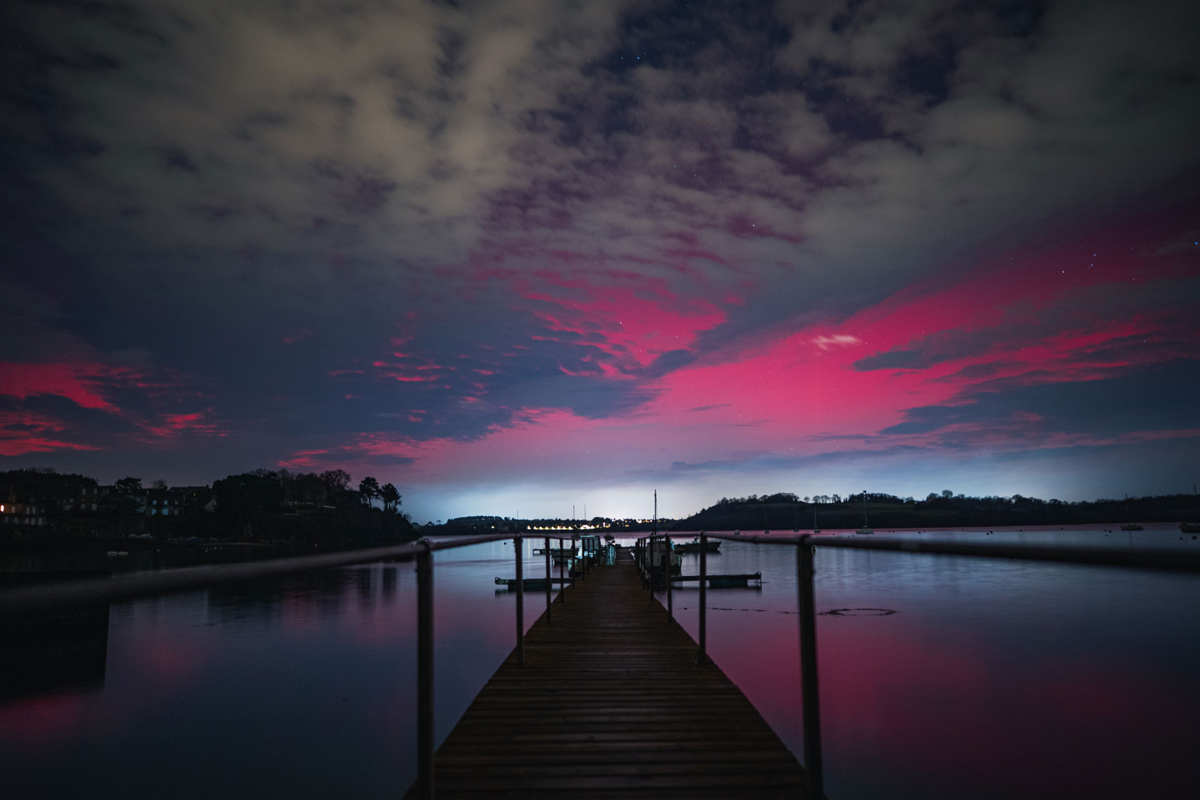 Aurores boréales à Saint-Malo en Bretagne au-dessus d’un ponton, avec des teintes roses et vertes dans le ciel nocturne.